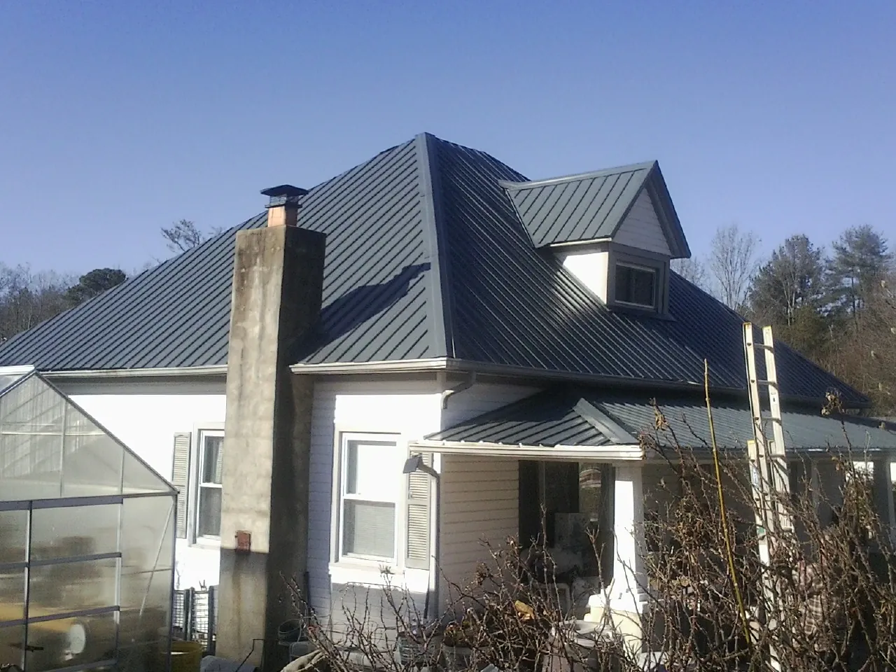 Dark blue standing seam metal roof on a white farmhouse with dormer — Slate & Tile Roof Repair by Roofing Brothers in Westborough