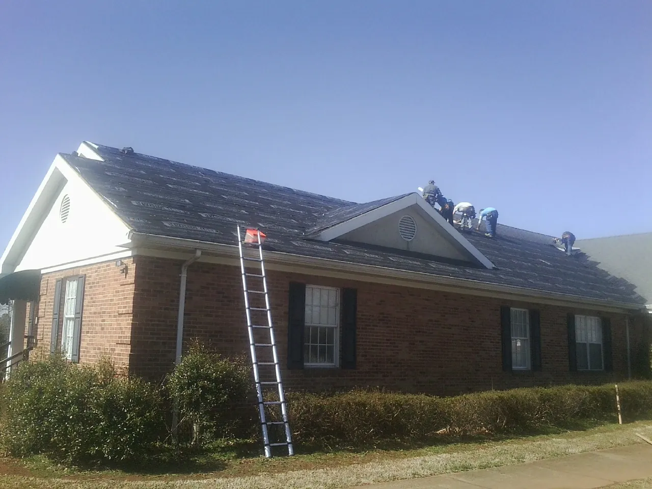 Crew tearing shingles off a brick ranch roof with a ladder set — Metal Roof Repair work by our crew in Westborough