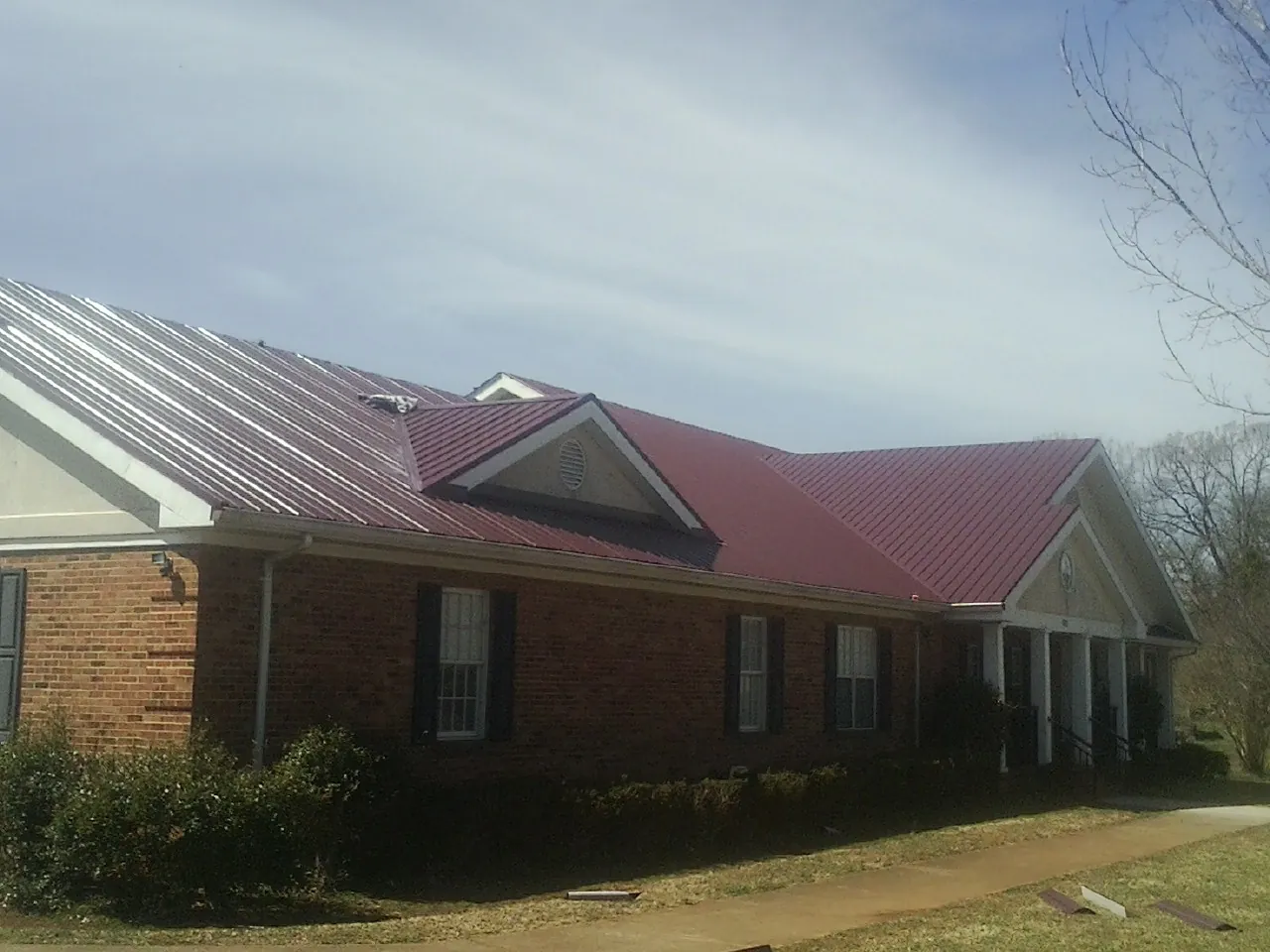 Red metal roof with gabled entries on a long brick building, from a Hail Damage Roof Repair job in Westborough