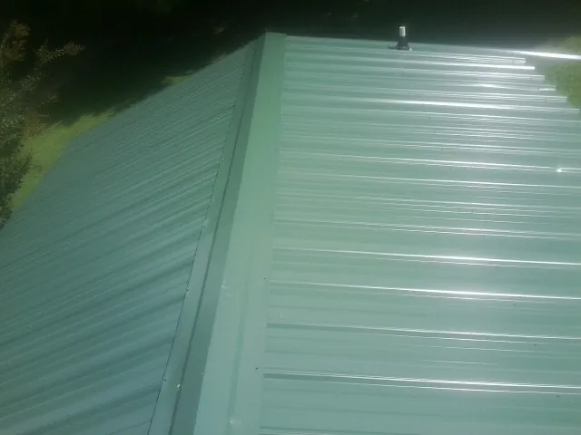 New green metal panels meeting at the ridge of a roof — Flat Roof Repair work by our crew in Westborough