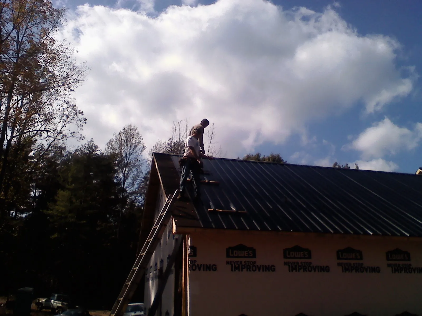 Roofer fastening dark metal panels high against a cloudy sky, from a Roof Inspection job in Westborough