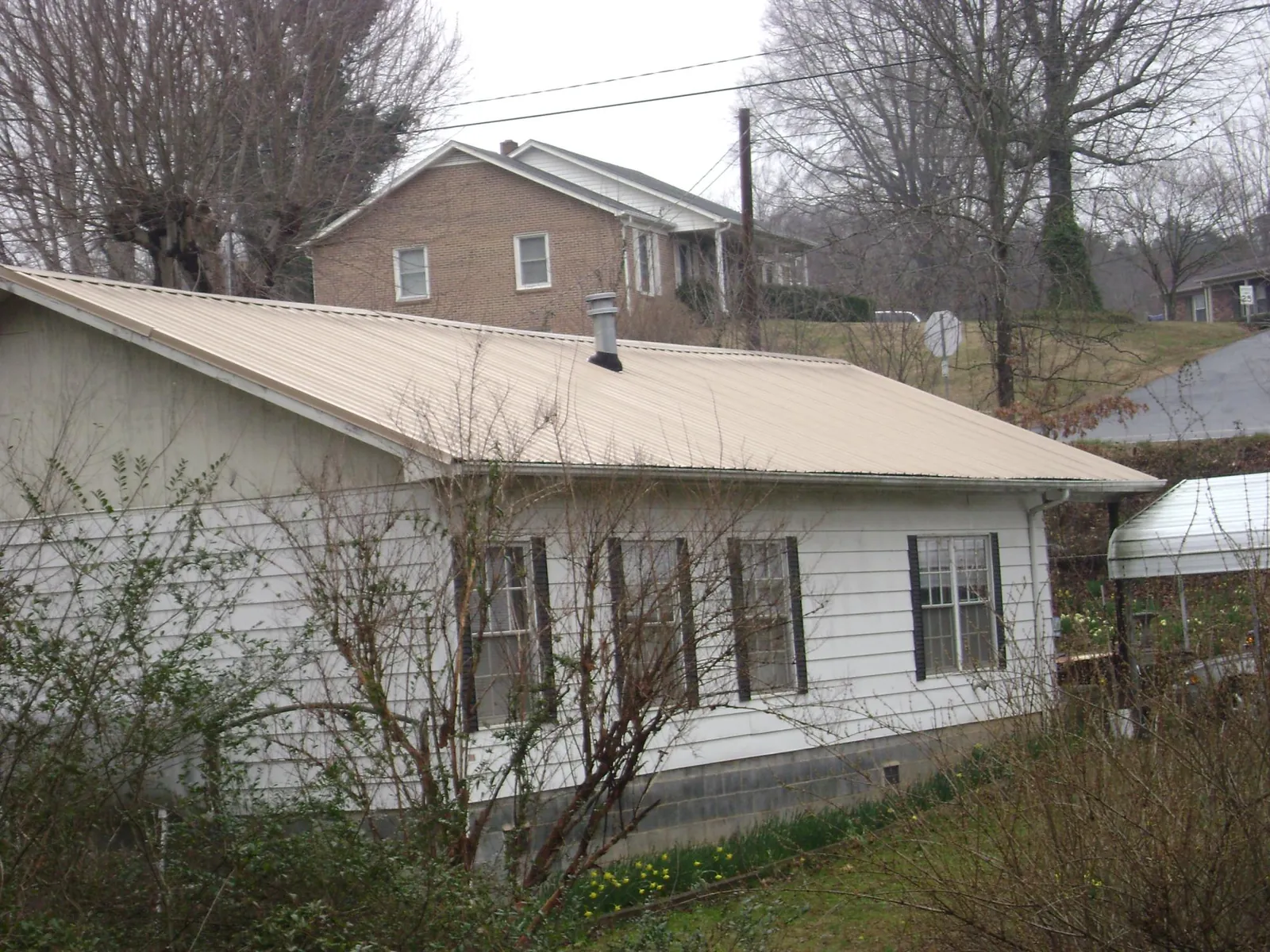 Tan metal roof on a white sided house set into a hillside — Commercial Roofing by Roofing Brothers in Westborough
