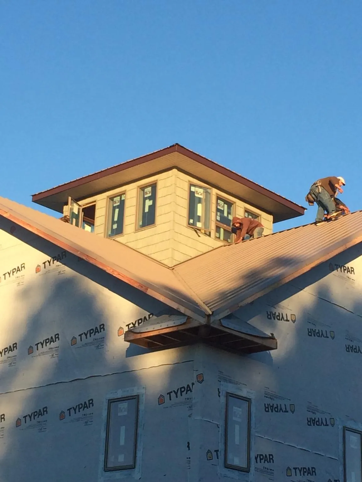 Roofers working around a rooftop cupola on a new metal roof at sunset — Roof Waterproofing in Westborough by Roofing Brothers